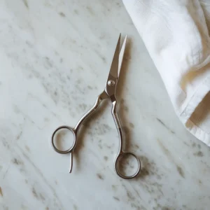 Close-up of stainless steel scissors on a marble surface next to a white towel.