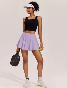 A woman wearing a lavender PINSPARK tennis skirt, styled with a flowy silhouette and high-waisted comfort, suitable for pickleball enthusiasts.